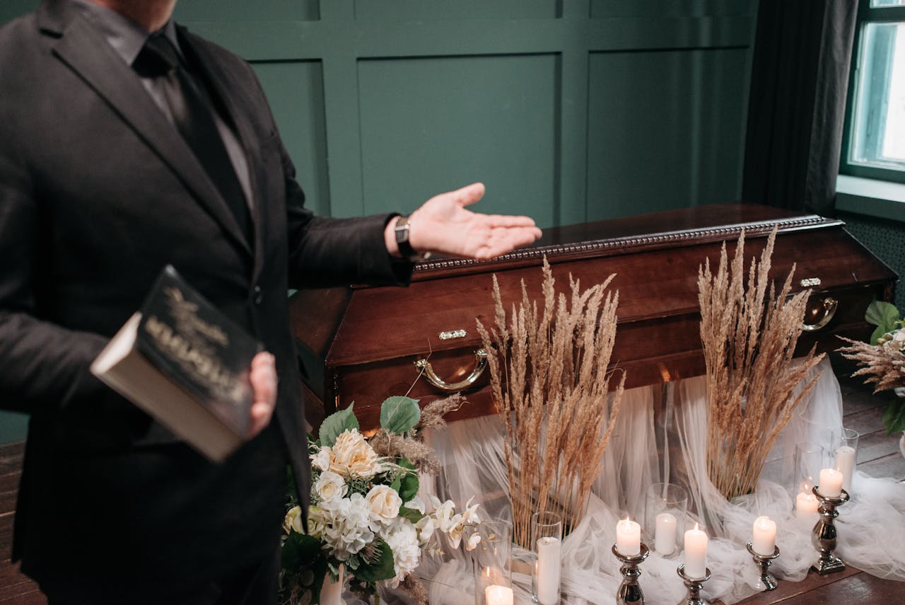 hero-about A respectful funeral setting with a closed coffin, flowers, and a man holding a book.